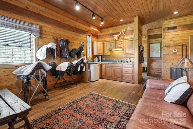 living area with track lighting, light wood finished floors, wooden walls, and wooden ceiling