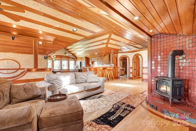 living room featuring lofted ceiling, light wood-type flooring, arched walkways, and a wood stove