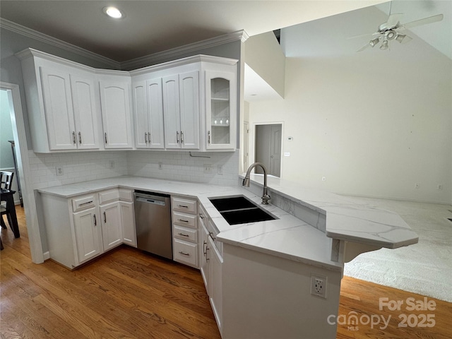 kitchen with stainless steel dishwasher, a sink, a peninsula, crown molding, and light stone counters