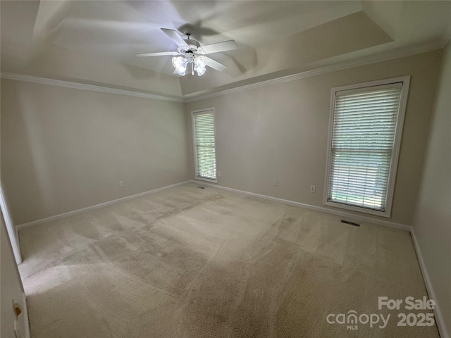 empty room with a tray ceiling, crown molding, ceiling fan, and healthy amount of natural light