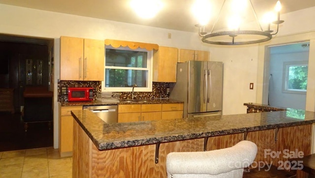 kitchen featuring appliances with stainless steel finishes, decorative backsplash, a sink, light tile patterned floors, and a chandelier