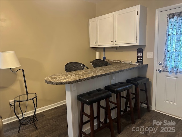 kitchen featuring dark wood finished floors, baseboards, a breakfast bar, and white cabinets