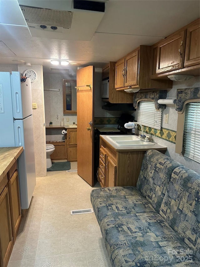 kitchen featuring freestanding refrigerator, a sink, and brown cabinetry