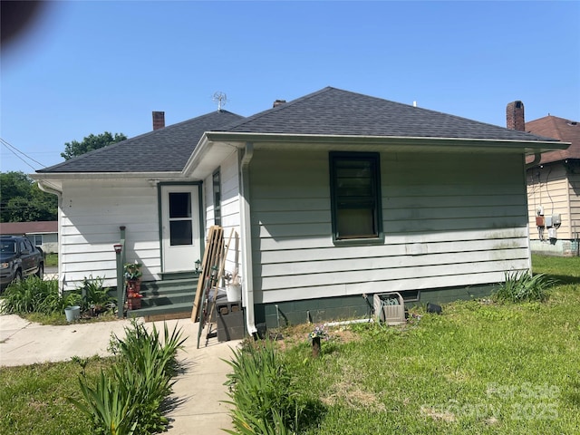 view of front of home with a shingled roof, a front lawn, and entry steps