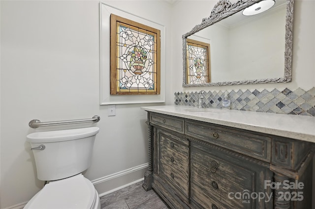 half bathroom with crown molding, baseboards, decorative backsplash, toilet, and vanity