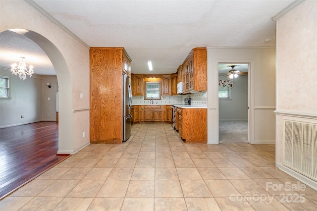 319 Glenhaven Dr, Charlotte, NC 28214 - kitchen with freestanding refrigerator, brown cabinetry, a ceiling fan, light countertops, and arched walkways