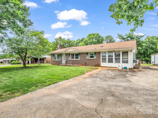 single story home featuring a chimney, brick siding, a front lawn, and driveway