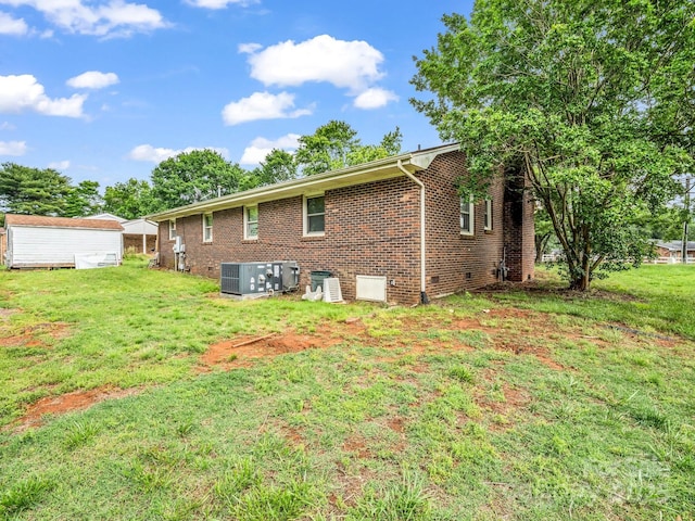 back of property with a yard, central AC unit, brick siding, and a storage unit