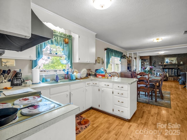 kitchen featuring a textured ceiling, wall chimney range hood, light countertops, a sink, and a peninsula