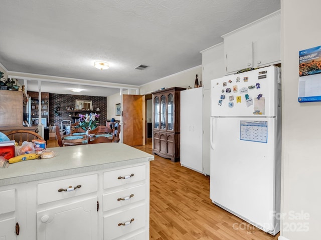 kitchen featuring freestanding refrigerator, a textured ceiling, light countertops, light wood-type flooring, and white cabinetry
