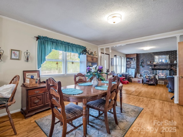 dining room with a textured ceiling, light wood-style floors, a brick fireplace, crown molding, and baseboards