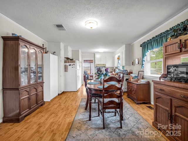 dining space featuring light wood-style floors, ornamental molding, and a textured ceiling