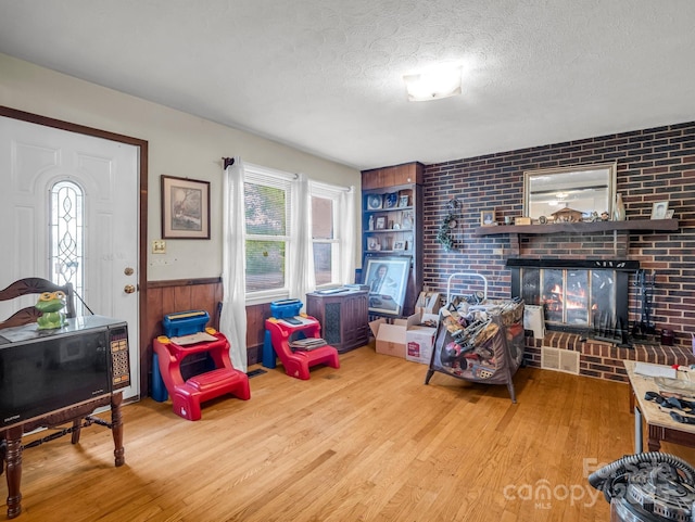 living room with wood finished floors, a textured ceiling, wainscoting, and a brick fireplace
