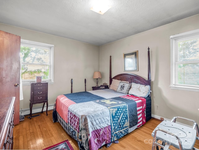 bedroom featuring a baseboard radiator, wood finished floors, multiple windows, and a textured ceiling