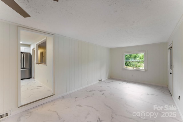 unfurnished room with light marble finish floors, a textured ceiling, and baseboards