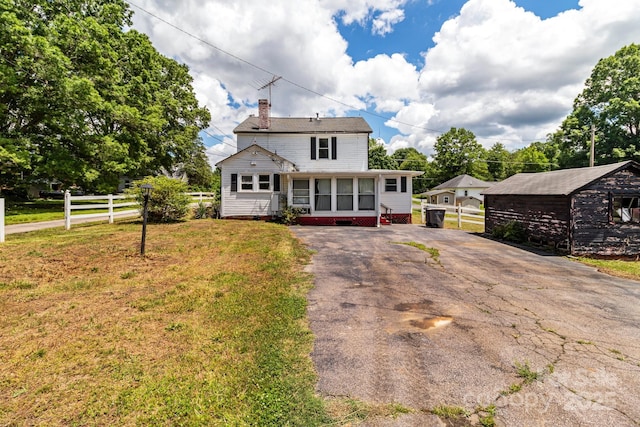 view of front facade featuring a chimney, driveway, a sunroom, and an outdoor structure