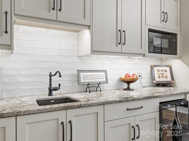 kitchen featuring beverage cooler, black microwave, a sink, backsplash, and light stone counters