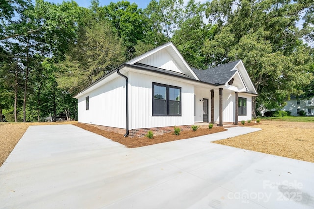 315 W Hoke St W, Landis, NC 28088 - modern inspired farmhouse with a porch, a shingled roof, concrete driveway, and view of wooded area