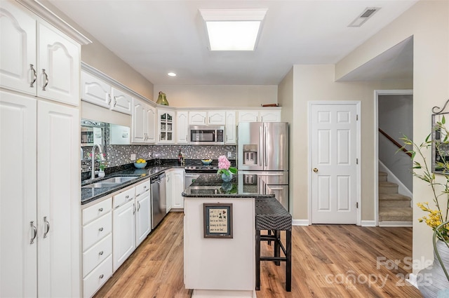 5208 Black Oak Ln, Waxhaw, NC 28173 - kitchen with stainless steel appliances, a sink, a kitchen bar, white cabinets, and light wood-type flooring