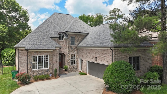 6132 Sharon Rd, Charlotte, NC 28210 - french provincial home featuring a shingled roof, driveway, an attached garage, and brick siding