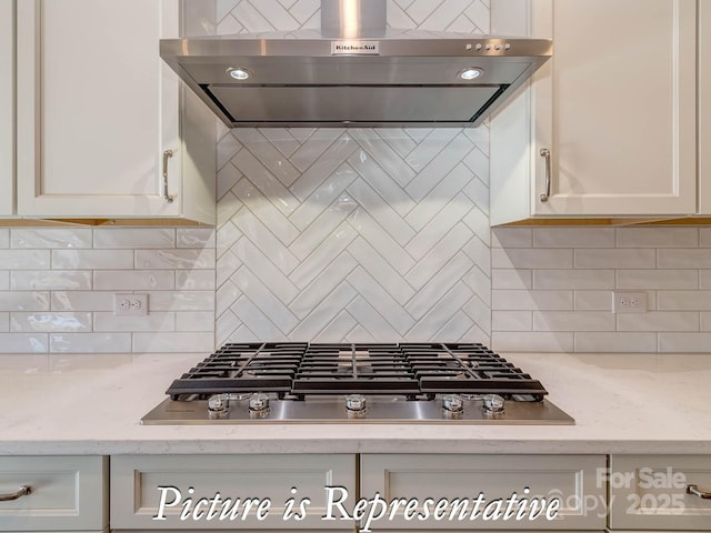 3439 Stags Leap Way, York, SC 29745 - kitchen featuring exhaust hood, stainless steel gas stovetop, backsplash, white cabinets, and light stone countertops