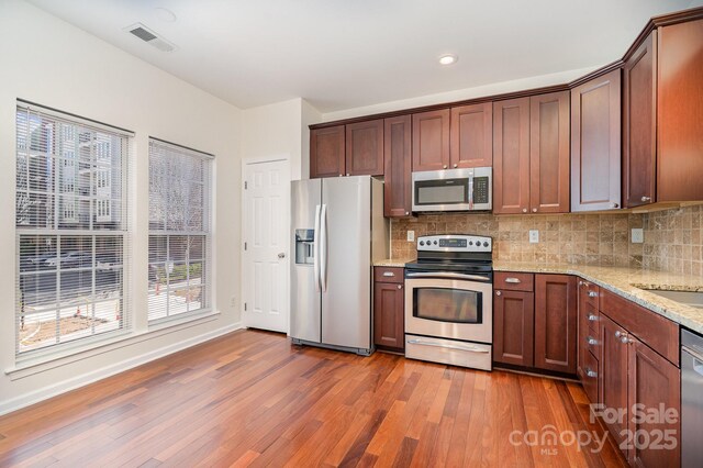 243 Lincoln St, Charlotte, NC 28203 - kitchen with stainless steel appliances, wood finished floors, decorative backsplash, light stone countertops, and baseboards