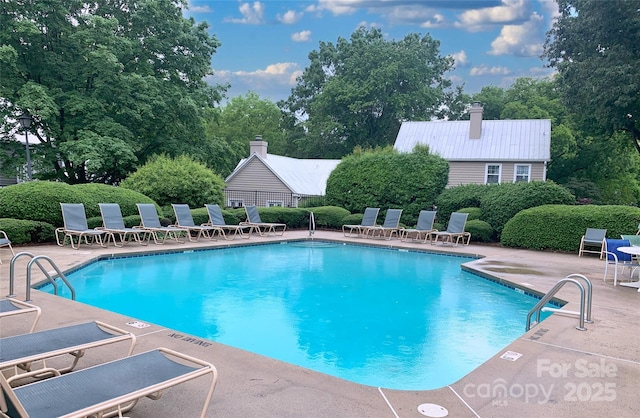 community pool with a patio area and view of wooded area