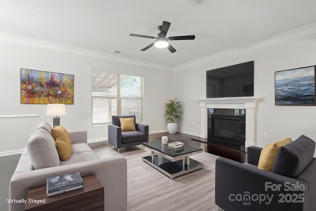 living area featuring crown molding, wood finished floors, a ceiling fan, baseboards, and a glass covered fireplace