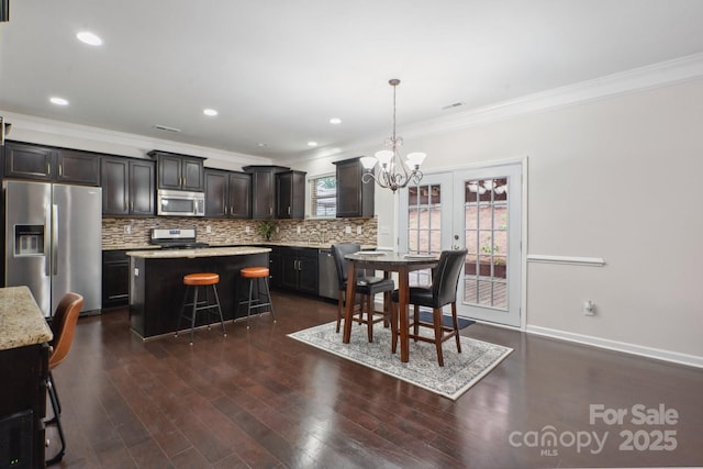 kitchen featuring stainless steel appliances, crown molding, a chandelier, tasteful backsplash, and dark wood-style flooring