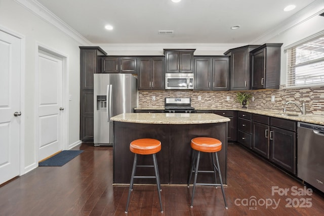 kitchen with stainless steel appliances, a center island, dark wood finished floors, ornamental molding, and a sink