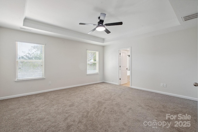 empty room with a raised ceiling, carpet, a ceiling fan, and baseboards