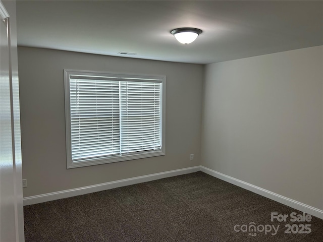 spare room featuring dark carpet and baseboards