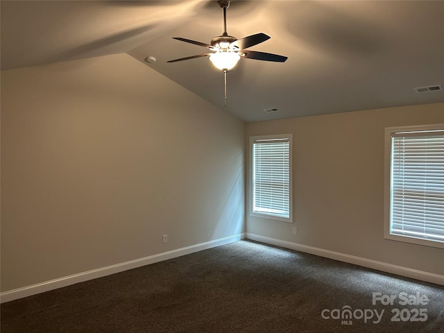 empty room with a ceiling fan, vaulted ceiling, dark colored carpet, and baseboards