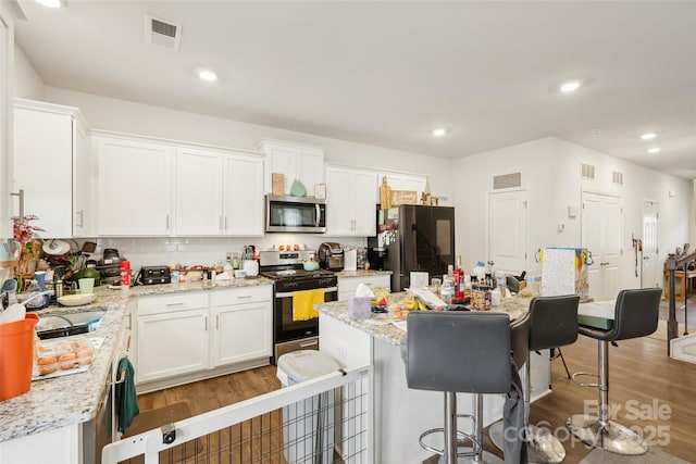3985 Village Blvd NW, Conover, NC 28613 - kitchen with stainless steel appliances, light wood-type flooring, a breakfast bar area, white cabinets, and decorative backsplash