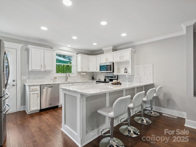 kitchen with stainless steel appliances, white cabinets, decorative backsplash, dark wood-style floors, and ornamental molding
