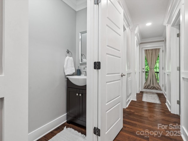 hall with ornamental molding, a sink, dark wood-type flooring, baseboards, and recessed lighting