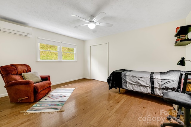 6334 Jacks Creek Rd, Burnsville, NC 28714 - bedroom featuring a wall mounted air conditioner, light wood-style flooring, baseboards, a ceiling fan, and a textured ceiling