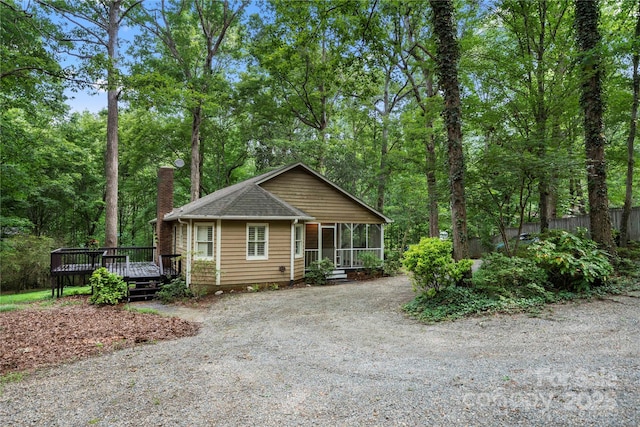 view of front of house featuring a sunroom, a chimney, a wooden deck, fence, and gravel driveway