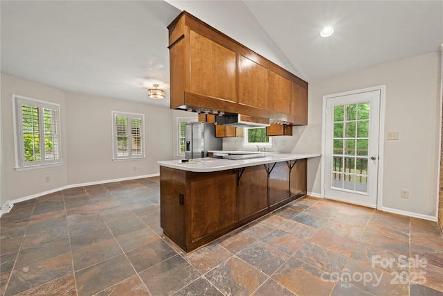 kitchen with stone tile floors, a peninsula, brown cabinets, stainless steel refrigerator with ice dispenser, and baseboards