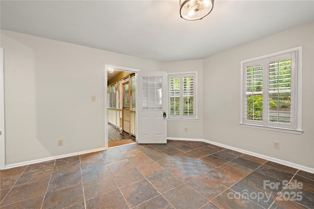 empty room featuring baseboards and stone tile floors