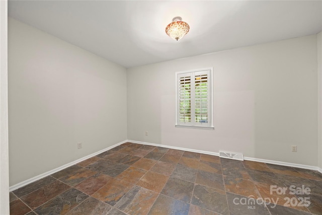 unfurnished room with stone tile flooring and baseboards