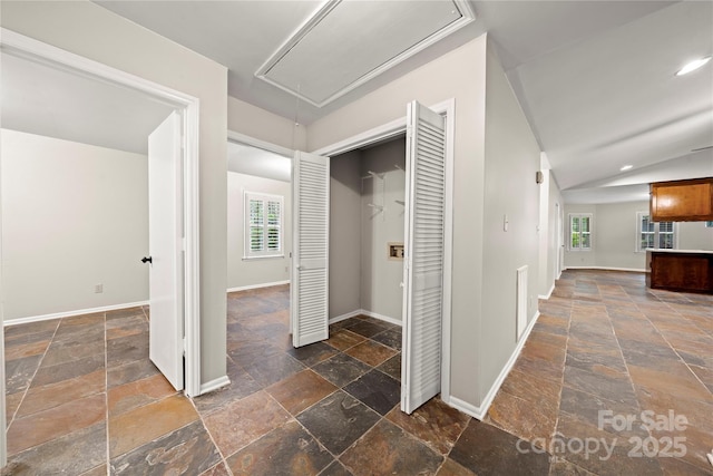 corridor with attic access, stone tile floors, healthy amount of natural light, vaulted ceiling, and recessed lighting