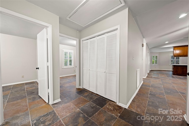 hall with stone tile flooring, attic access, healthy amount of natural light, baseboards, and recessed lighting