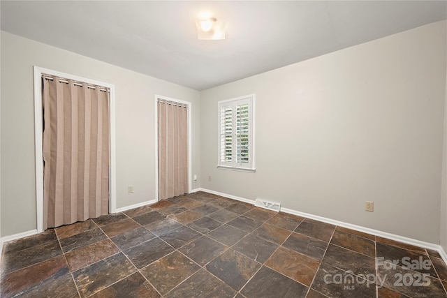 unfurnished bedroom featuring baseboards, stone tile flooring, and two closets