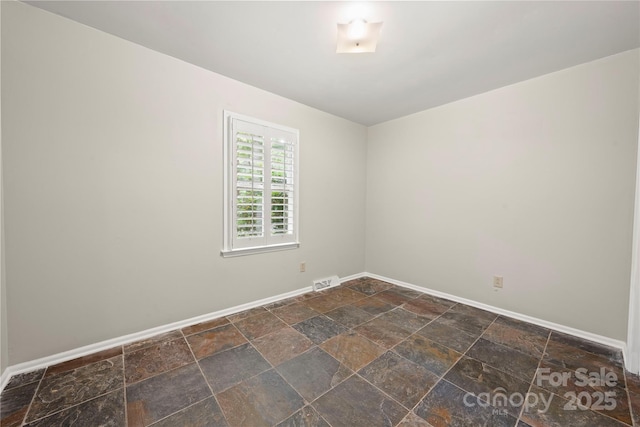 spare room with baseboards and stone tile flooring