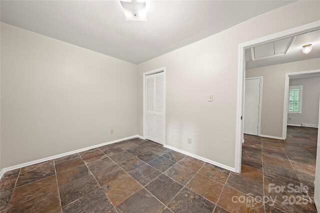 spare room featuring stone tile floors, attic access, and baseboards