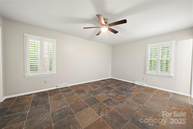 spare room with a ceiling fan, dark stone finish floors, and baseboards