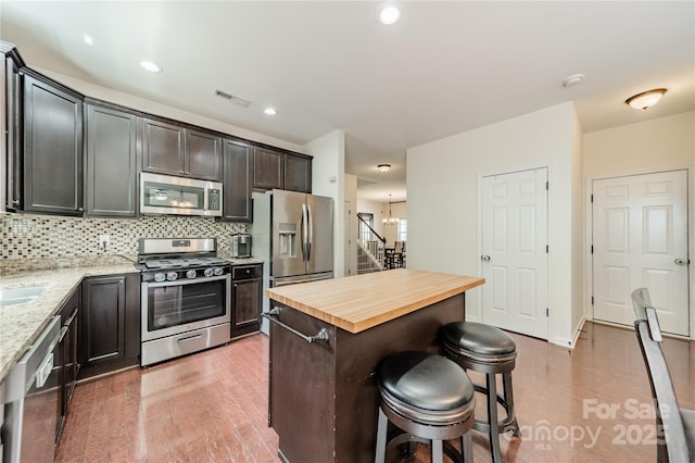 7650 W Berkeley Rd, Denver, NC 28037 - kitchen featuring appliances with stainless steel finishes, a breakfast bar area, light wood finished floors, decorative backsplash, and light stone counters
