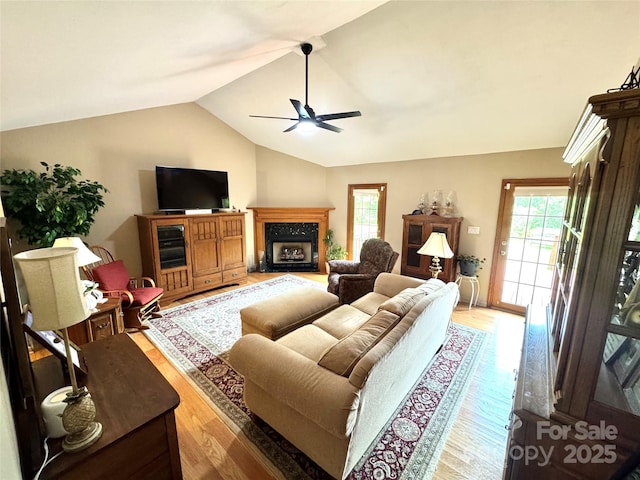 living room featuring a ceiling fan, plenty of natural light, lofted ceiling, light wood-type flooring, and a high end fireplace
