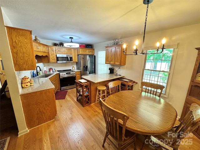 kitchen with appliances with stainless steel finishes, light wood-style floors, a peninsula, and brown cabinetry